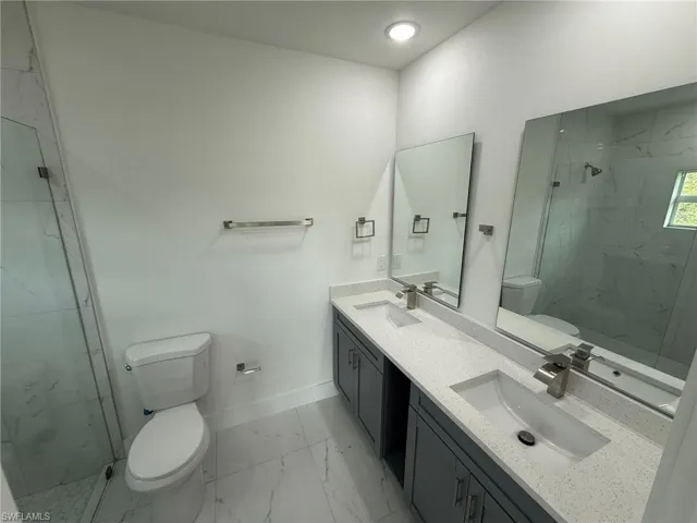 Bathroom featuring a marble finish shower, double vanity, and light marble finish flooring