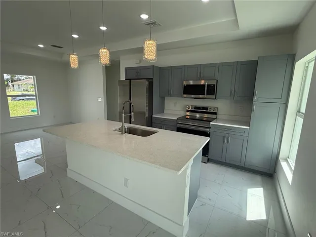 Kitchen featuring stainless steel appliances, pendant lighting, recessed lighting, light marble finish flooring, and a center island with sink