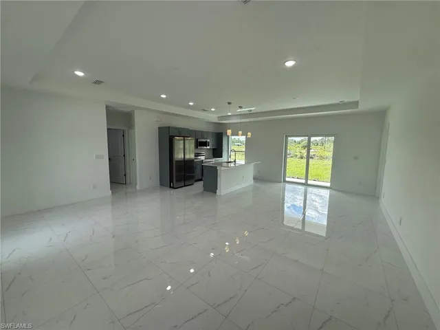 Unfurnished living room with light marble finish flooring, a tray ceiling, and recessed lighting
