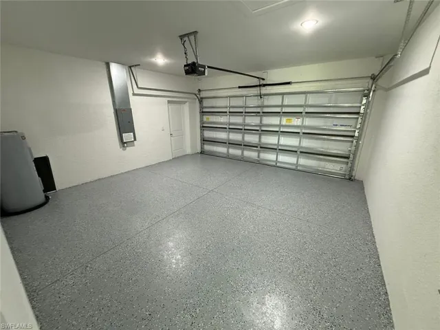 Garage featuring electric panel, a garage door opener, and water heater