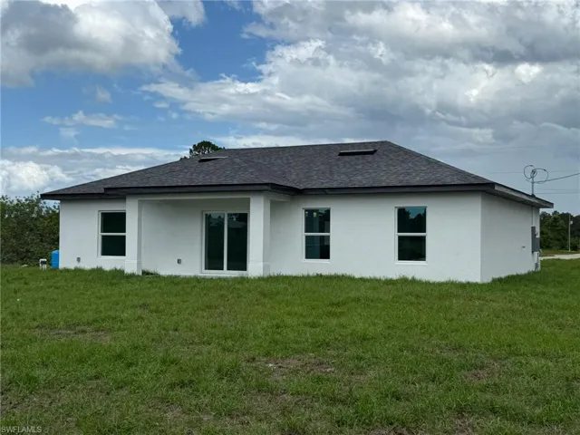 Rear view of house with a shingled roof, stucco siding, and a lawn