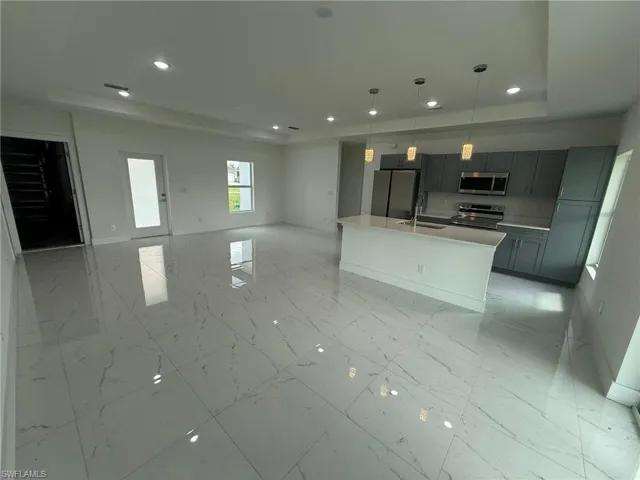 Kitchen with recessed lighting, a center island with sink, decorative light fixtures, open floor plan, and light marble finish flooring