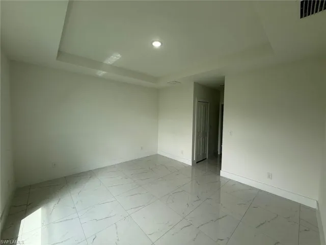 Spare room featuring a tray ceiling, light marble finish flooring, and recessed lighting