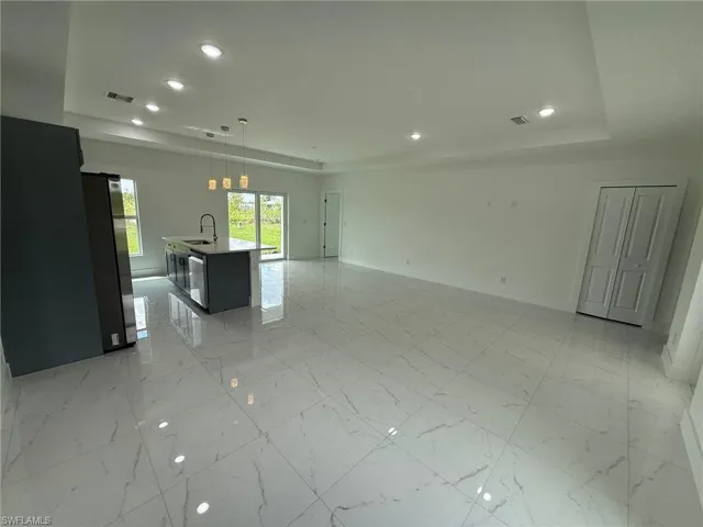 Unfurnished living room featuring recessed lighting, a tray ceiling, and light marble finish flooring