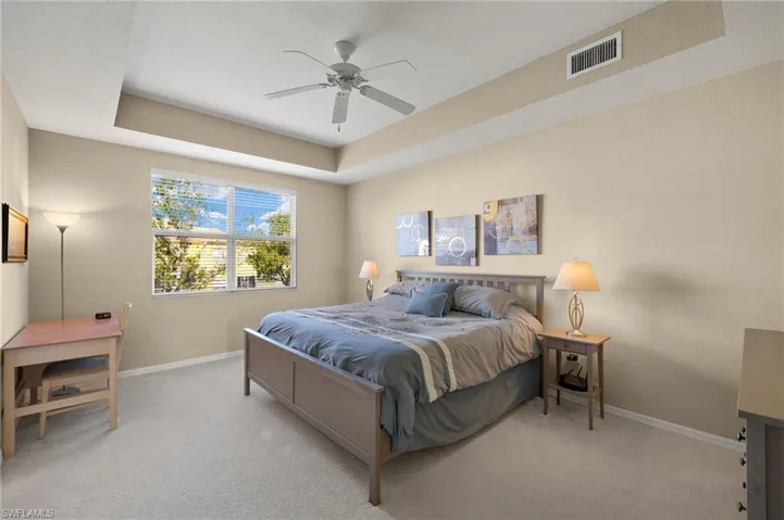 Carpeted bedroom with ceiling fan and a tray ceiling