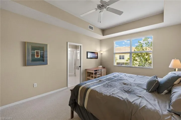 Bedroom with light carpet, connected bathroom, a tray ceiling, and ceiling fan