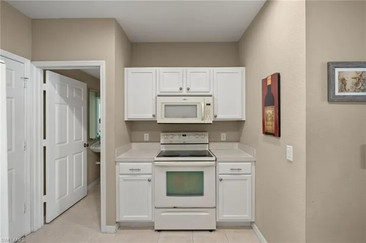 Kitchen with light tile patterned floors, white appliances, and white cabinets