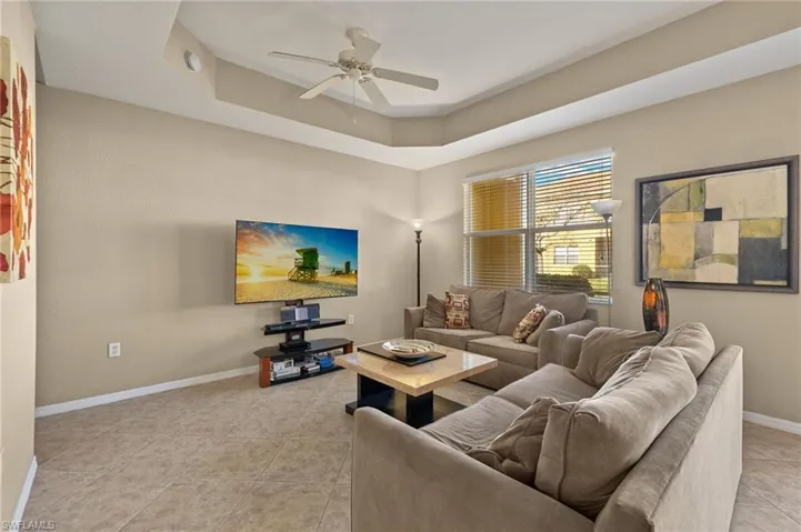Living room featuring ceiling fan, a tray ceiling, and light tile patterned floors