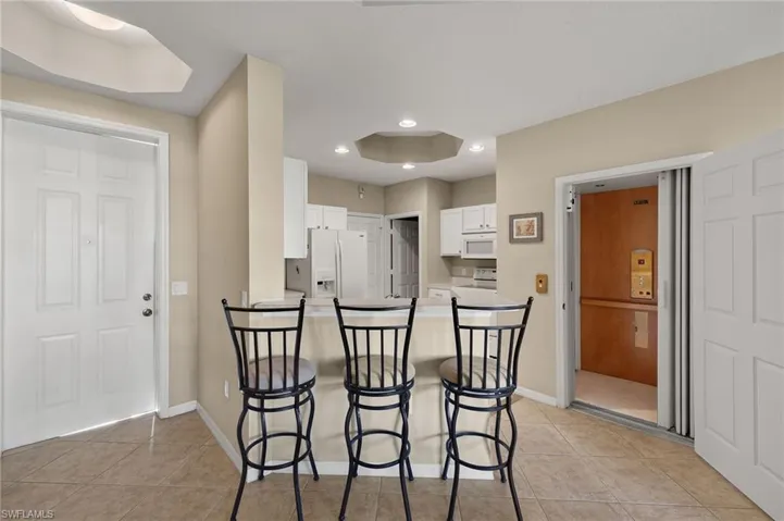 Kitchen featuring light tile patterned flooring, a breakfast bar area, kitchen peninsula, white appliances, and white cabinets