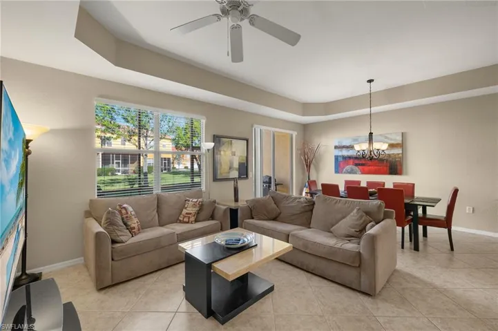 Living room featuring ceiling fan with notable chandelier, light tile patterned floors, and a tray ceiling
