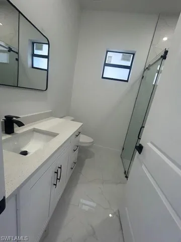 Bathroom featuring vanity, a marble finish shower, and light marble finish flooring