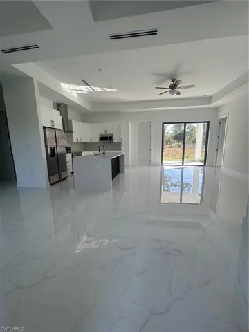 Kitchen featuring open floor plan, white cabinets, fridge, an island with sink, and range hood