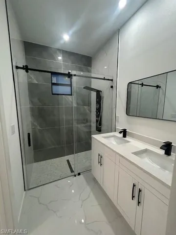Bathroom with a marble finish shower, light marble finish floors, and double vanity