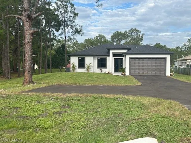 View of front of house with stucco siding, asphalt driveway, a front lawn, and an attached garage