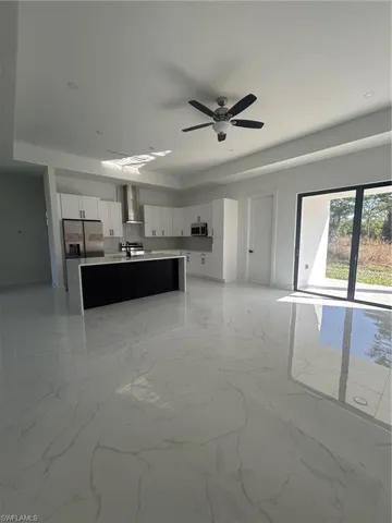 Kitchen with white cabinetry, open floor plan, light marble finish flooring, and ventilation hood