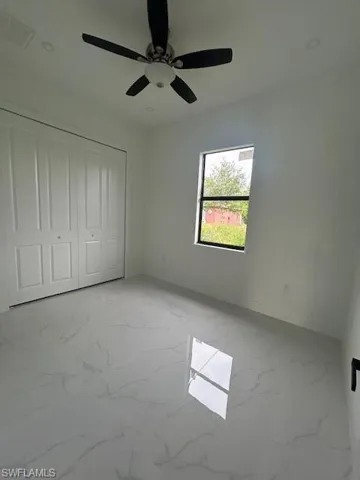 Unfurnished bedroom featuring light marble finish floors, a ceiling fan, and a closet