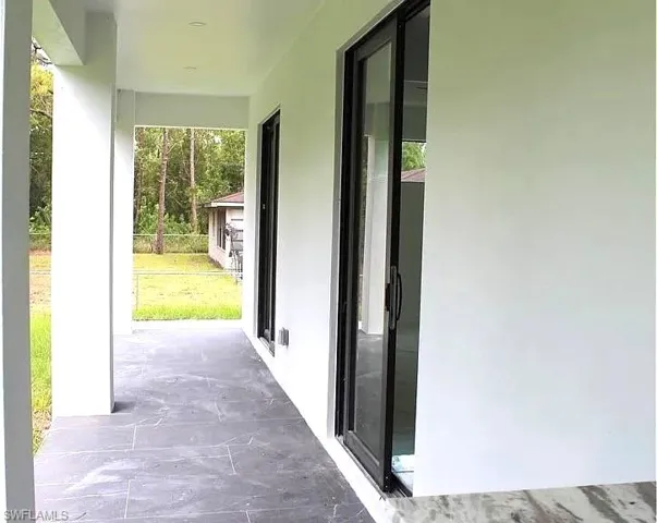 Covered patio featuring rectangular floor tiles in a dark finish, white columns, a white ceiling with recessed lighting, and black-framed sliding glass doors