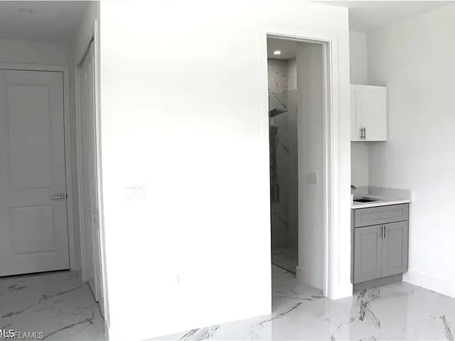 Contemporary interior featuring white walls, large format tile flooring with dark veining, a built-in vanity with grey cabinetry, a white upper cabinet, and a shower enclosure with tiled walls