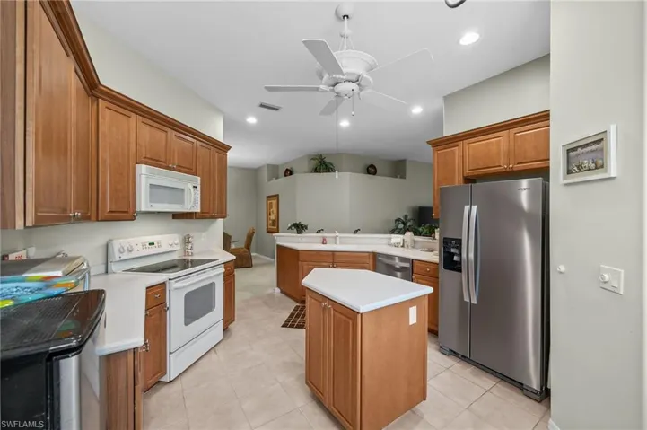 Kitchen featuring appliances with stainless steel finishes, a peninsula, light countertops, brown cabinets, and a kitchen island