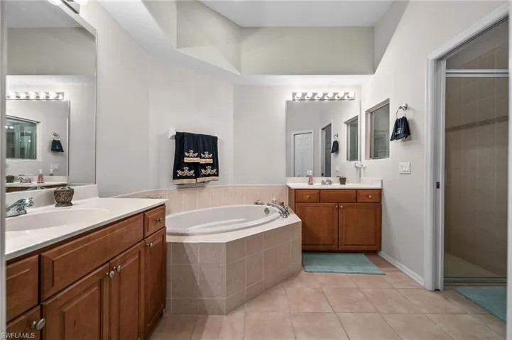 Bathroom with a bath, light tile patterned flooring, a stall shower, and two vanities
