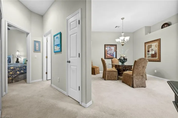 Hall with light carpet and a chandelier