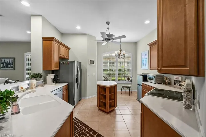 Kitchen with brown cabinetry, light tile patterned flooring, a chandelier, hanging light fixtures, and a ceiling fan