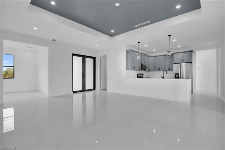 Open-concept living space featuring high-gloss tile flooring, a tray ceiling with recessed lighting, and a modern kitchen with grey cabinetry, stainless steel appliances, and a breakfast bar