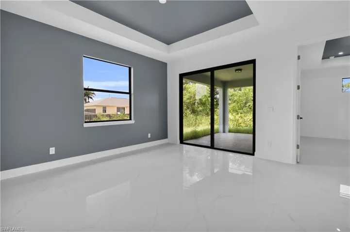 Spacious interior featuring a recessed tray ceiling, large format tile flooring, a window with outdoor scenery, and sliding glass doors opening to a covered patio