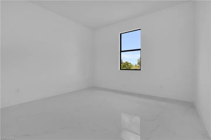 Bright interior space featuring a single window with black trim, white walls, white baseboards, and large format white tile flooring with subtle veining