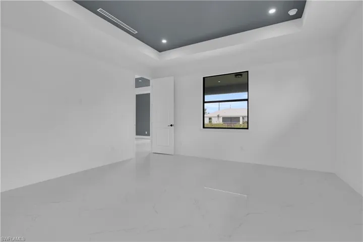 Spacious interior room featuring a tray ceiling with recessed lighting, large window with black framing, white panel door, and light-toned tile flooring