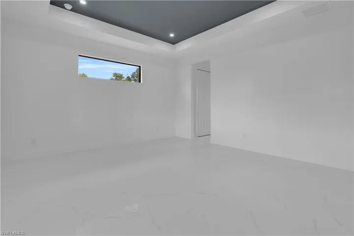 Spacious room featuring white tile flooring, a painted tray ceiling, recessed lighting, and a horizontal window
