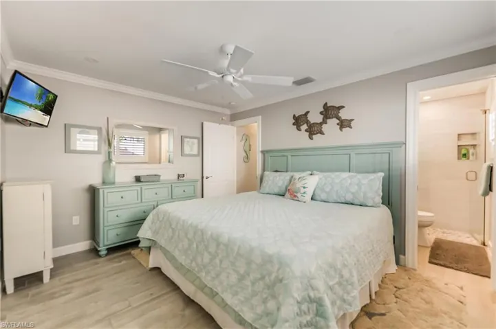 Bedroom featuring light wood-style floors, ornamental molding, ensuite bathroom, and ceiling fan