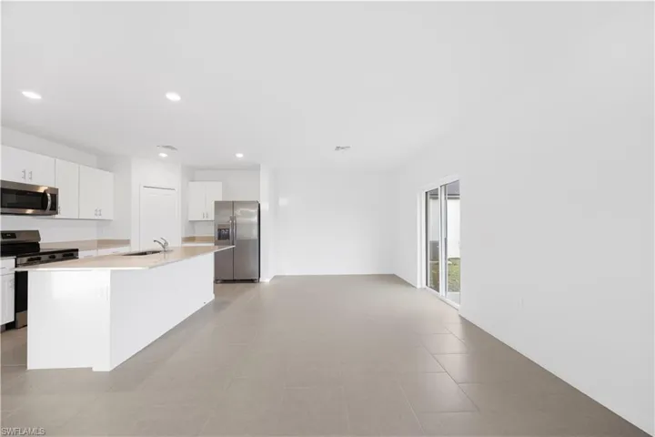 Kitchen with stainless steel appliances, white cabinets, a center island with sink, and recessed lighting