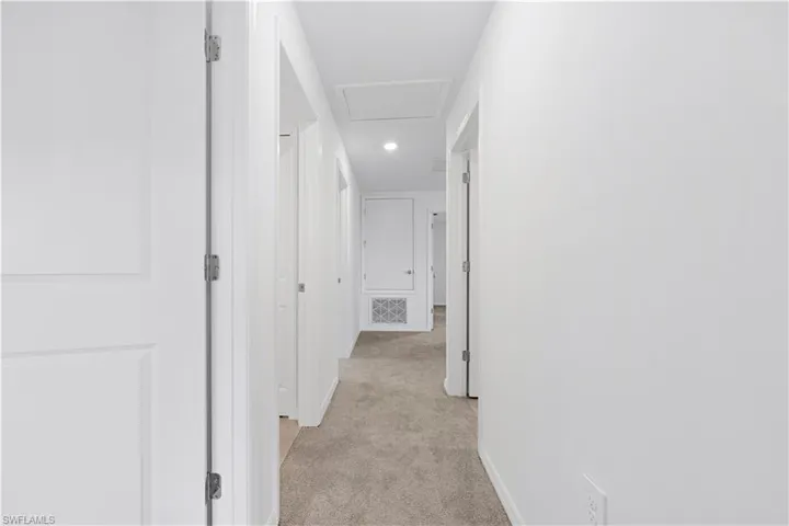 Hallway with light colored carpet and baseboards