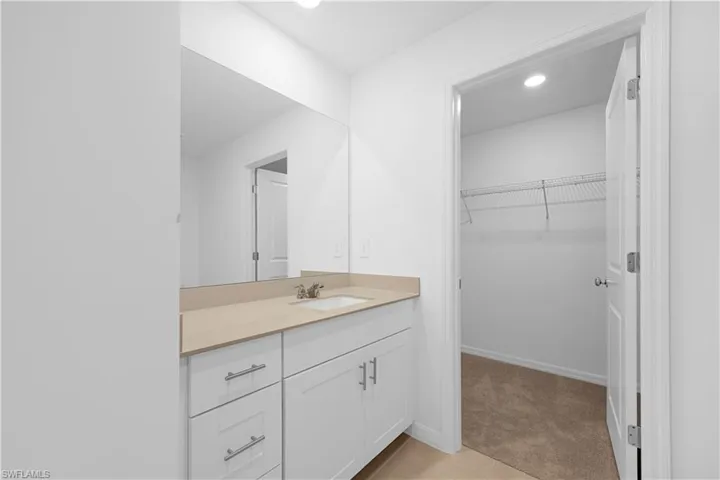 Bathroom with vanity, recessed lighting, a walk in closet, light colored carpet, and light tile patterned floors
