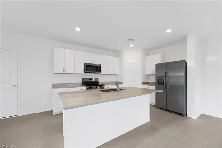 Kitchen with stainless steel appliances, white cabinetry, an island with sink, recessed lighting, and light tile patterned flooring