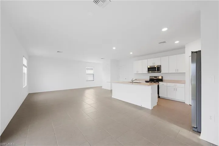 Kitchen with light countertops, white cabinets, stainless steel appliances, light tile patterned floors, and a center island with sink