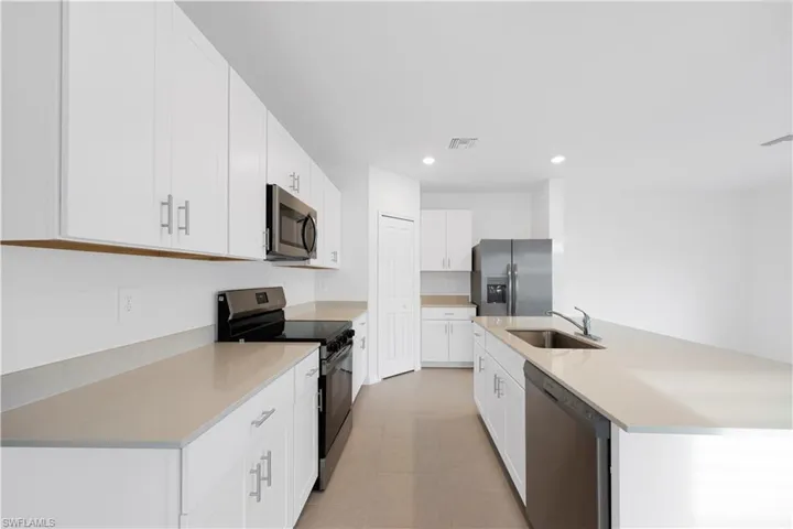 Kitchen featuring stainless steel appliances, a kitchen island with sink, white cabinetry, and recessed lighting