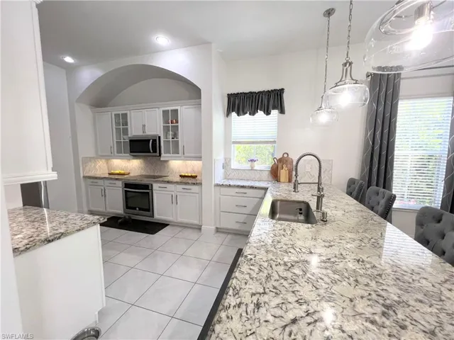 Kitchen featuring tasteful backsplash, white cabinetry, appliances with stainless steel finishes, light stone countertops, and sink