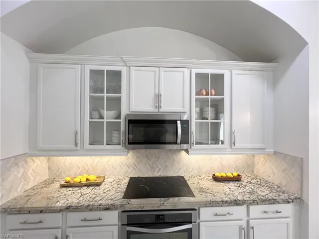 Kitchen with tasteful backsplash, white cabinetry, light stone countertops, and stainless steel appliances