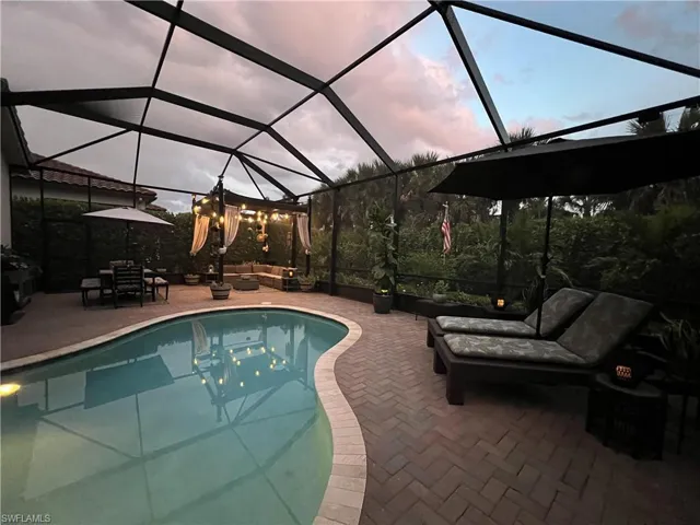 Pool at dusk featuring glass enclosure and a patio area