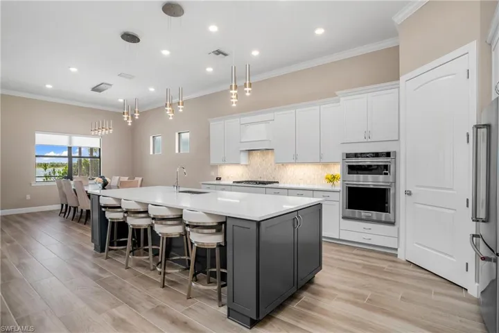 Kitchen is a chef's dream with oversize island, upgraded white cabinetry, walk-in pantry, natural gas cooktop, upgraded appliances, and designer lighting.
