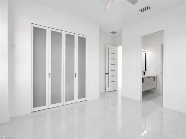 Unfurnished bedroom featuring connected bathroom, ceiling fan, light marble finish floors, and a closet