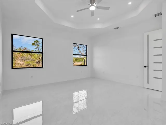 Empty room with a ceiling fan, a raised ceiling, and recessed lighting