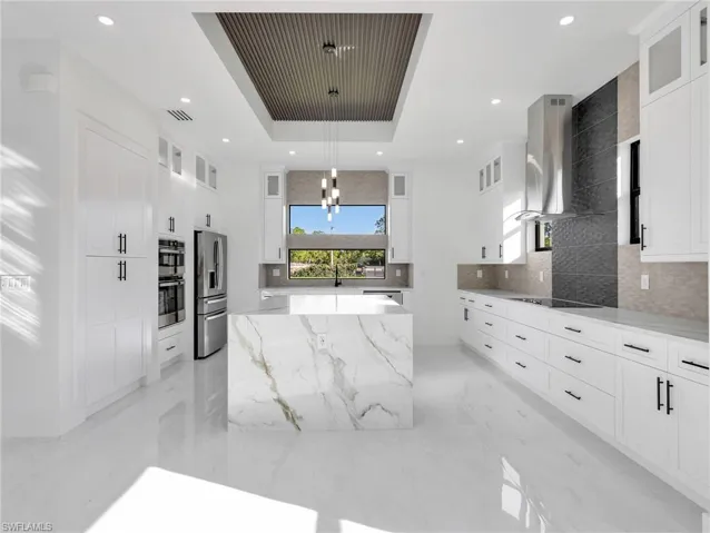 Kitchen featuring glass fronted cabinets, a kitchen island, light stone countertops, hanging lights, and stainless steel appliances
