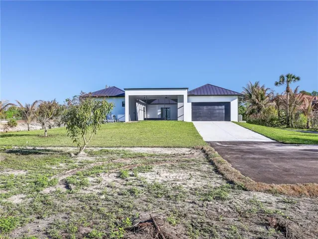 Modern home with a standing seam roof, a front yard, driveway, and stucco siding