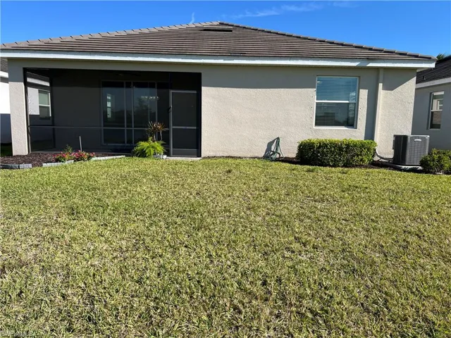 Rear view of property with stucco siding, a lawn, a sunroom, and a tile roof