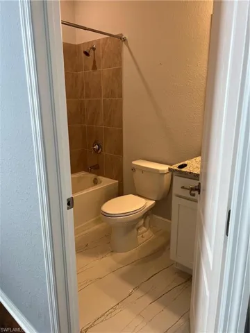 Full bath featuring a textured wall, vanity, light marble finish flooring, and shower / bath combination