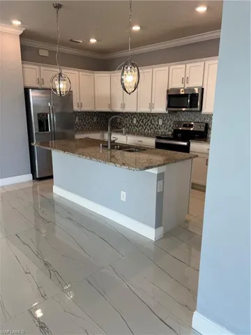 Kitchen featuring range, dark stone countertops, stainless steel refrigerator, white cabinets, and pendant lighting