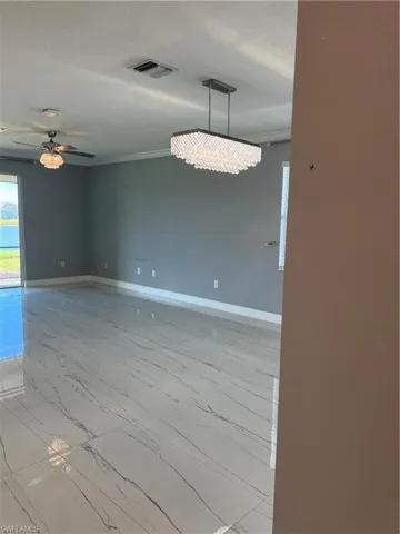 Spare room featuring ceiling fan, healthy amount of natural light, light marble finish flooring, and suspended lighting